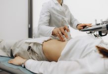 Closeup of male doctor moving ultrasound probe on pregnant woman's stomach in hospital